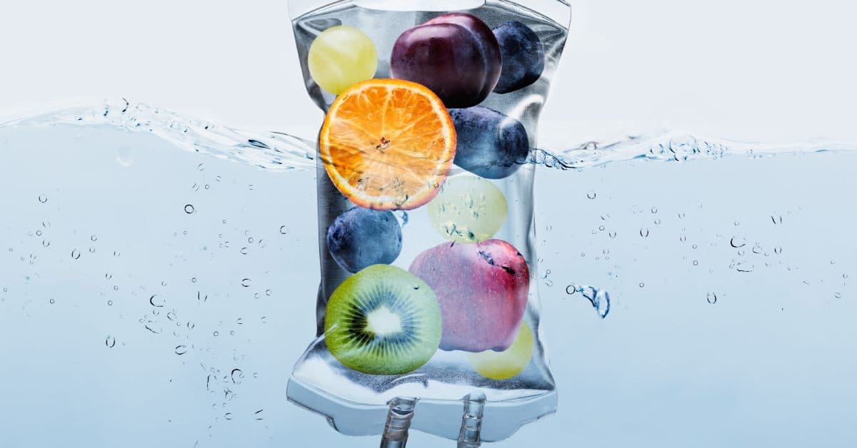An IV therapy bag with a bunch of fresh fruit inside, including kiwis, orange slices, grapes, and an apple.